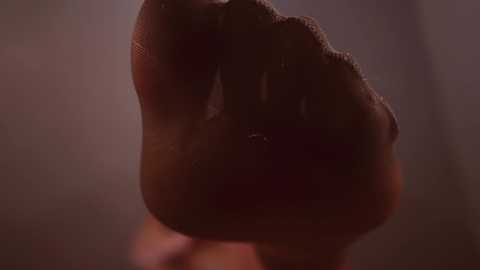 Media: Video of a close-up, partially blurred, dark-skinned hand gripping a smooth, reddish-brown object, possibly a weapon, against a dimly lit, out-of-focus background. The image is grainy and has a cinematic, dramatic atmosphere.