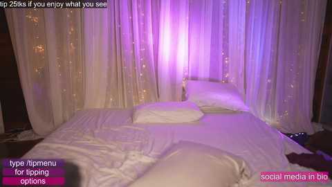 Media: Video of a bedroom with white drapes, a bed with white sheets, and a purple light source. Text on the image reads, \"Enjoy what you see.\