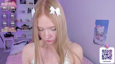 Media: Video of a blonde, fair-skinned young woman with white bow headband, wearing a light-colored bra. Background shows a pink room with a Hello Kitty poster, white shelves, and a soft pink blanket.