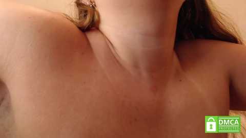 Media: A close-up video of a light-skinned woman's bare upper chest and neck, with visible tan lines and slight skin texture, showing a slightly reddened neck. Her shoulder-length brown hair is partially visible.