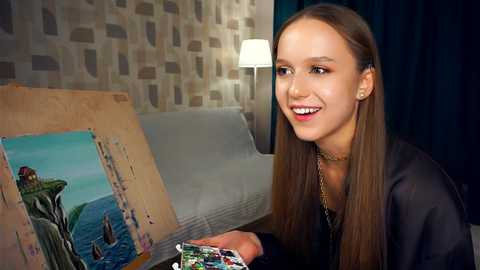 Media: Video of a smiling, light-skinned woman with long brown hair, wearing a black top, holding a colorful magazine. Background features a beige-patterned wall, a grey couch, and a dark curtain.