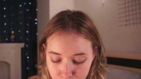 Media: Video of a young Caucasian woman with light brown hair, closed eyes, and a pimple on her forehead. Background shows a softly lit room with a dark curtain and a white shelf with a candle.