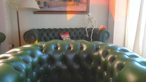 Media: Video of a vintage green leather tufted sofa with a skull decoration, framed painting, beige curtains, and a floor lamp in a cozy, warmly lit living room.