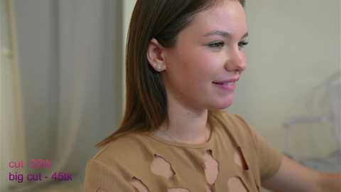 Media: Video of a smiling young woman with straight, shoulder-length brown hair, wearing a beige top with a large heart-shaped hole, against a blurred indoor background. Text in the corner reads \"curvy girl big bust- 45k.\