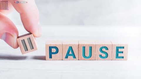 Media: Video of a hand holding a wooden block with the word \"Pause\" on it, standing on a light wooden floor. The background is blurred and white, creating a minimalistic, modern aesthetic.