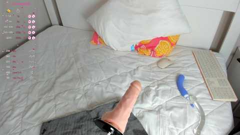 Media: Video of a neatly made bed with white sheets, a colorful pillow, and a laptop. A hand holding a blue vibrator and a book lies on the bed.