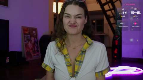 Media: A video of a woman with curly hair, wearing a yellow plaid shirt and sunglasses, smiling in a dimly lit room with gaming equipment and posters in the background.