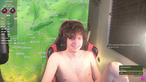 Media: Video of a young, shirtless, fair-skinned, slim, and smiling Caucasian male with brown hair, sitting in a red and black gaming chair, playing a video game in a dimly lit room.