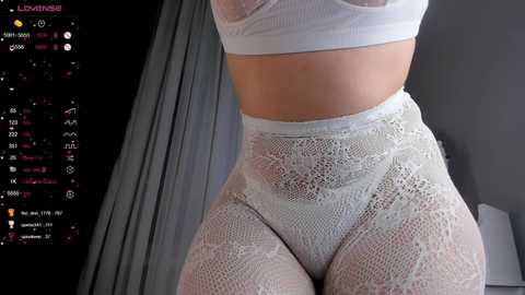 Media: Video of a woman wearing white lace lingerie, including a bra and high-waisted panties, against a dark background with a digital screen displaying various social media icons.