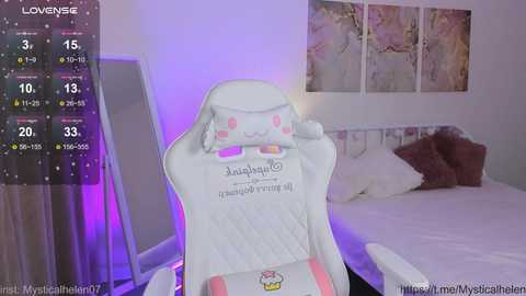 Media: Video of a white gaming chair with a pink and white cushion, placed in a dimly-lit bedroom with a white bed and purple lighting.