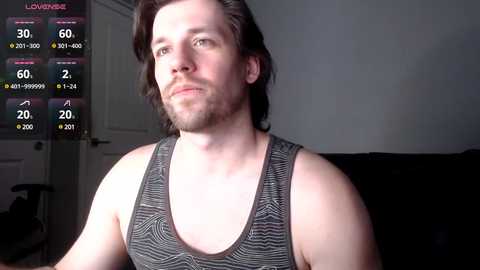 Media: Video of a fit, bearded man in a black tank top, standing in a dimly lit room with a virtual reality headset displaying a game interface.