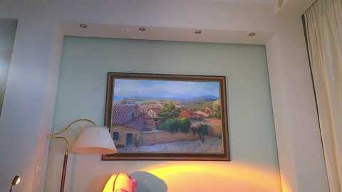 Media: A video of a cozy bedroom corner featuring a framed landscape painting, a white lamp, and a soft yellow light illuminating the scene.