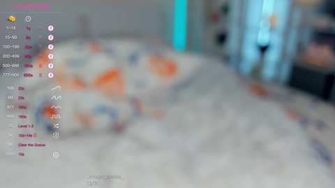 Media: A blurred, digital image of a bedroom with a bed covered in colorful bedding, featuring a person in the background, possibly a child. The room is bright with a blue light source.