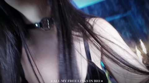 Media: Video of a young woman with long, dark hair, wearing a black choker, in a dimly lit room with blue and white hues.