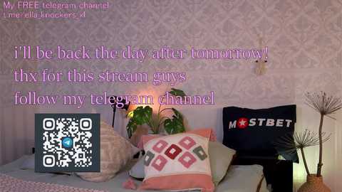 Media: Video of a cozy bedroom with a pink floral wallpaper, featuring a bed with multiple pillows, a black \"MOSTBET\" pillow, and a QR code overlay with text.