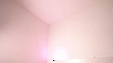 Media: Video of a minimalist, unfinished room with smooth, light beige walls. The space is sparse, with only a few small holes and a faint pink glow near the top left corner. The room has a clean, modern aesthetic.