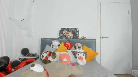 Media: Video of a white room with a bed adorned with plush toys, including a panda, penguin, and a red bear, against a white wall and closed door.