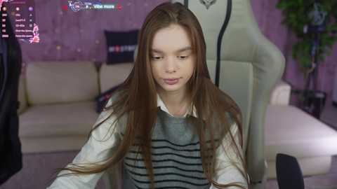 Media: A video shows a young girl with long brown hair in a grey sweater, sitting in a gaming chair, surrounded by a pink, sparkly wall and gaming equipment.