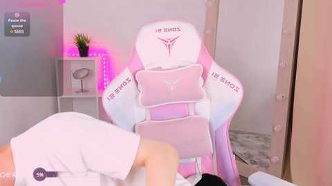 Media: Video of a young woman in a white T-shirt, lying face down on a pink gaming chair with \"IBIS\" branding, in a softly lit, minimalist room with a mirror, plants, and pink LED lights.