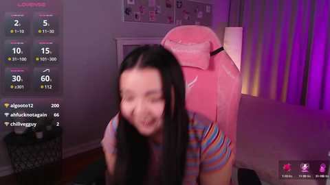 Media: A video of an Asian woman with long black hair, wearing a striped shirt, playing a game on a pink gaming chair in a dimly lit room with purple lighting.