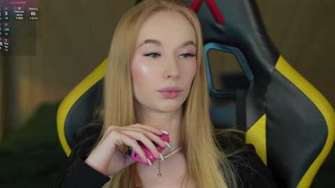 Media: A video of a young blonde woman with fair skin, wearing a black top, applying makeup in a gaming chair with a black and yellow design.