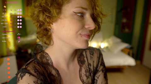 Media: Video of a fair-skinned woman with curly red hair, wearing a sheer black lace robe, looking contemplative in a dimly lit bedroom with a bed and green walls.