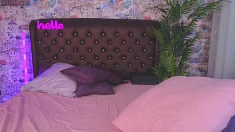 Media: Video of a cozy bedroom with a tufted, dark brown headboard, pink bedding, lavender pillows, and a colorful, abstract mural background.