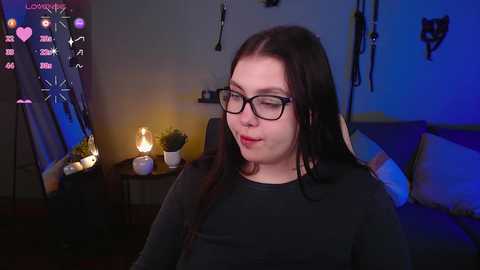 Media: A video of a young woman with long, dark hair and glasses in a dimly-lit room with a lit candle, BDSM gear, and a mirror.