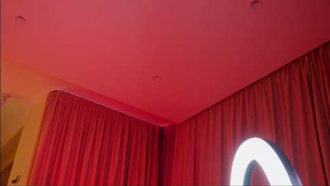 Media: Video of a corner room with red curtains, a circular light fixture, and a yellow wall, creating a cozy, intimate atmosphere.