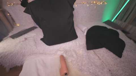 Media: Video of a person wearing a black hat, lying on a white shag rug, with a visible erect penis. Background features a bed with white bedding and fairy lights.