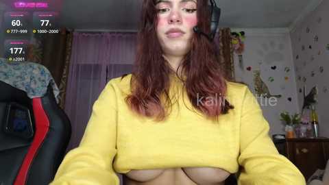 Media: Video of a woman with long red hair wearing a yellow crop top, revealing her large breasts, in a cluttered bedroom.