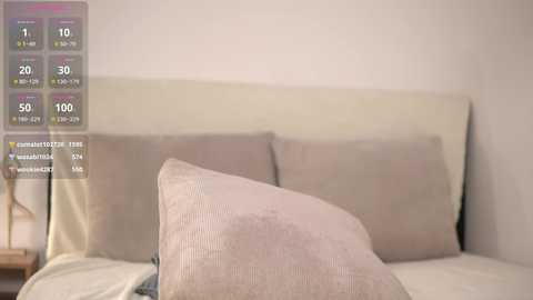 Media: Video of a minimalist bedroom featuring a beige headboard, two beige pillows, and a light-colored bedspread, with a digital weather display overlaid on the left side.