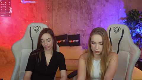 Media: Video of two young women, one with long brown hair, the other with long blonde hair, seated in gaming chairs with Razer logos. Background features a red and purple-lit wall and gaming setup.