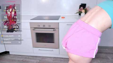 Media: A video captures a woman in pink shorts bending over in a modern kitchen, with an oven and white cabinets in the background.