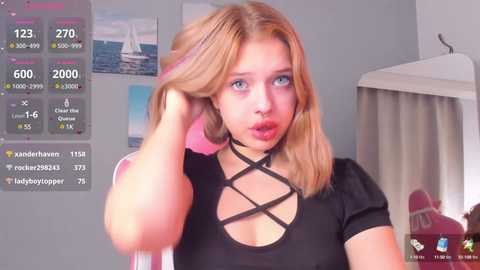 Media: Video of a young, fair-skinned woman with blonde hair, wearing a black, crisscross-patterned top, playfully pulling her hair. Background includes a sailboat picture, white curtain, and social media metrics overlay.