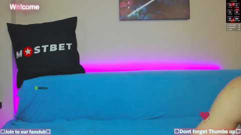 Media: Video of a person lying on a blue bed with a \"MOSTBET\" pillow and a pink neon strip light on the wall, with a \"Welcome\" watermark and text in the bottom corners.