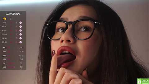 Media: Video of a dark-haired woman with large glasses and red lipstick, biting her finger, set against a blurred background, with a \"LOVE\" overlay and a \"DMM\" watermark.