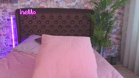 Media: Video of a modern bedroom with a plush, tufted dark brown headboard, pink pillows, a vibrant green plant, and a colorful abstract wall.