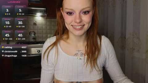 Media: Video of a young, fair-skinned woman with long, reddish-brown hair, smiling, wearing a white crop top in a kitchen. A virtual thermometer and chat bubbles appear on the left.