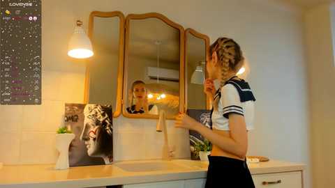 Media: Video of a young woman with braided hair, wearing a sailor-themed top and black skirt, applying lipstick in a modern bathroom with a tiled wall, mirror, and a black-and-white photo of a woman.