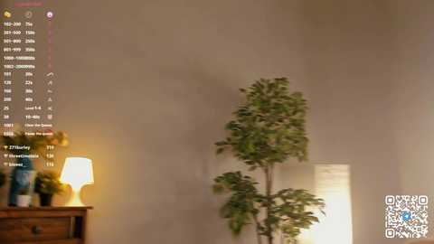 Media: Video of a dimly lit room with a tall, leafy indoor plant, a wooden side table, and a warm yellow lamp casting soft light. A digital clock with a calendar display is visible on the wall.