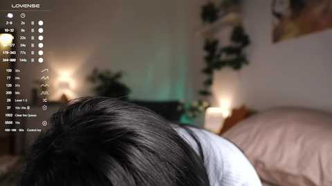 Media: Video of a woman with dark hair lying on a bed, viewed from behind, in a dimly lit room. A digital calendar and clock display on the left side.