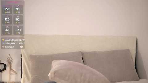 Media: Video of a minimalist bedroom with beige headboard, two pillows, and a small, white decorative lamp on the left side.