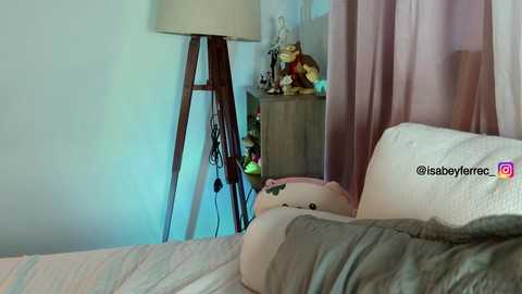 Media: Video of a cozy bedroom with a beige lamp on a wooden stand, a stuffed bear, and soft pastel curtains, creating a warm, inviting atmosphere.