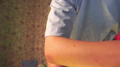 Media: A video of a person's arm, wearing a light blue shirt, with a small black bug on the skin, in a grassy outdoor setting.