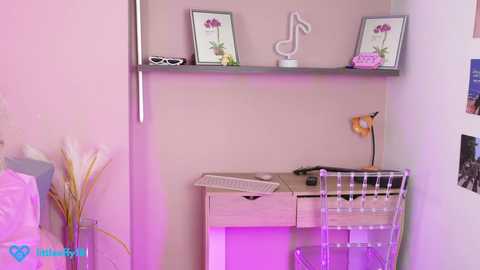 Media: Video of a minimalist, pink-lit room with a wooden desk, glass chair, two framed flower pictures, and a white music note sculpture.