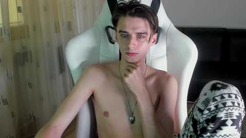 Media: Video of a young, shirtless Caucasian male with pale skin, wearing a black and white patterned hat, sitting in a white gaming chair.