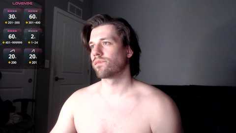 Media: Video of a shirtless, light-skinned man with medium-length brown hair, looking contemplative. Background includes a dark couch and a closed door. The image has an overlay of video game statistics.