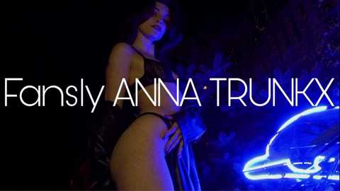 Media: Video of a dark-haired woman in a black, sheer lace bra and thong, posing provocatively outdoors at night. Neon blue car lights illuminate her. Text overlay reads \"Farsly Anna Trunkxx.\