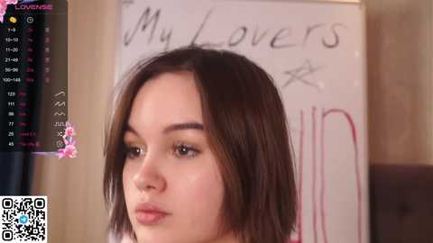 Media: A video shows a young Asian woman with straight, shoulder-length brown hair, wearing a neutral expression. Behind her, a whiteboard with the phrase \"My lovers\" written in cursive is visible. The image has a QR code in the bottom left corner.